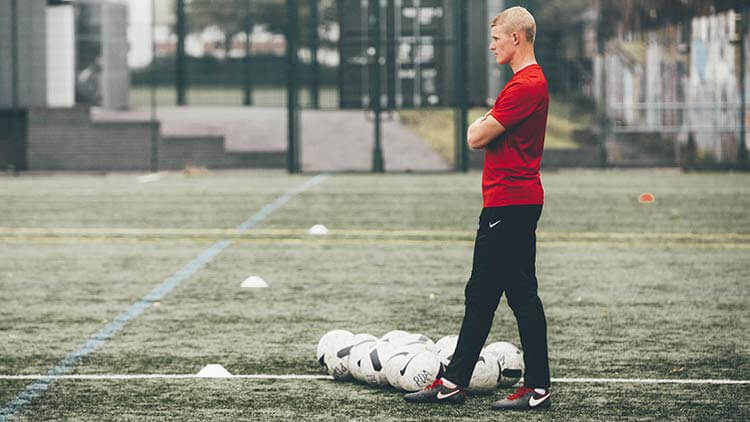 A man in training gear standing with a pile of training footballs